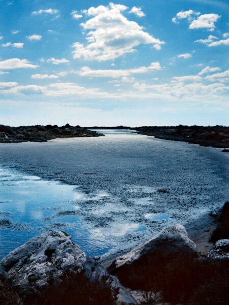 Fine art picture showing a salt pan close to the sea with pointy rocks in the foreground